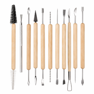 Rang d'outils de sculpture à manche en bois avec embouts métalliques (spatules, crochets, ciseaux) et deux brosses sur la gauche.